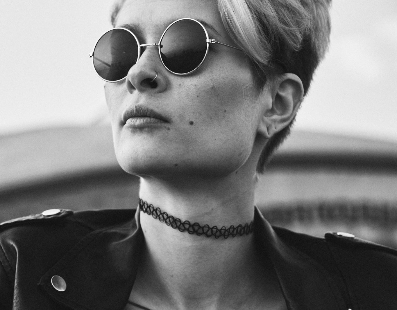 Eine Frau Eine selbstbewusst junge Frau mit einer runden Sonnenbrille und einem Piercing im rechten Nasenloch.